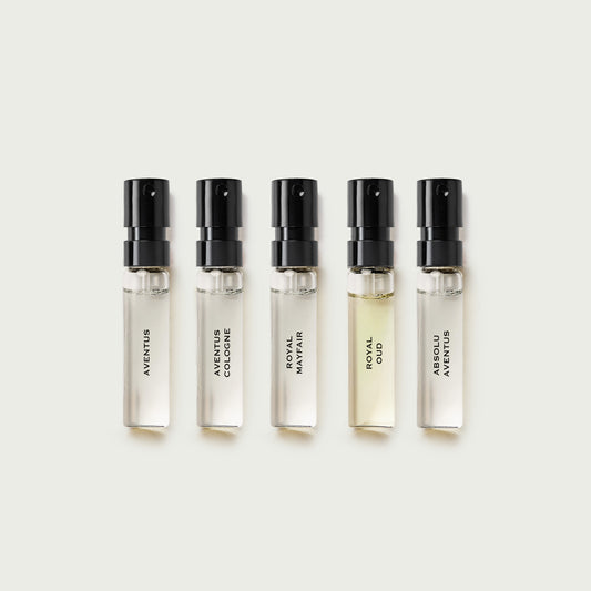 Five small perfume bottles with black caps on a light beige background