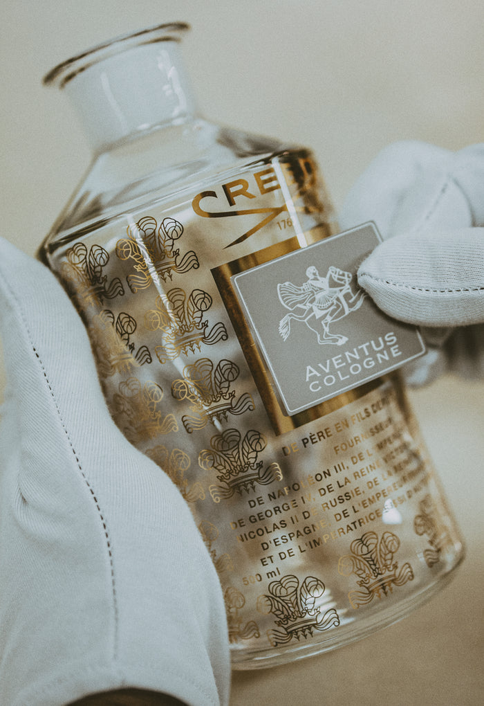A white glove man applying a label to a large flacon of Creed Aventus Cologne